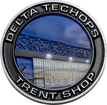 Circular challenge coin featuring Delta TechOps Trent Shop text around a blue and silver depiction of an industrial hangar facility.