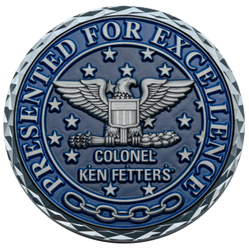 A circular blue challenge coin featuring a silver eagle with a shield, stars, and the text Colonel Ken Fetters Presented for Excellence.