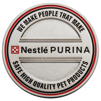 Silver challenge coin featuring the Nestlé Purina logo and a red outer border with inscribed text.